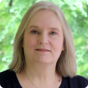 Julie has shoulder length, light coloured hair and wears a navy top and is smiling towards the camera outside Awen office.